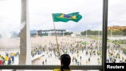 Yon patizan ansyen Prezidan Jair Bolsonaro flote drapo Brezil la pandan yon manifestasyon kont Prezidan Luiz Inacio Lula da Silva devan Palman Nasyonal la nan Brasilia, kapital peyi Brezil, 8 Janvye 2023.