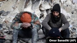 People react as they sit on the wreckage of collapsed buildings, in Aleppo, Syria, Tuesday, Feb. 7, 2023. (AP Photo/Omar Sanadiki)