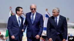 Prezidan Joe Biden kanpe bo kote Premye Minis Israelyen Yair Lapid a dwat, epi Prezidan Isaac Herzog, a goch, apre li rive nan ayewopo Ben Gurion nan, Mekredi 13 Jiye, 2022 nan Tel Aviv.