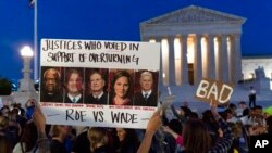 FILE - A demonstrator holds up a a sign with pictures of Supreme Court Justices Clarence Thomas, Brett Kavanaugh, Samuel Alito, Amy Coney Barrett, and Neil Gorsuch, as people protest outside of the U.S. Supreme Court, May 3, 2022.