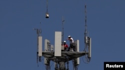 Workers install 5G telecommunications equipment on a T-Mobile tower in Seabrook, Texas, May 6, 2020.