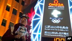 A supporter of the 2022 Beijing Winter Olympics poses for photos with a countdown clock as it crosses into the 100 days countdown to the opening of the Winter Olympics in Beijing, China, Oct. 26, 2021.