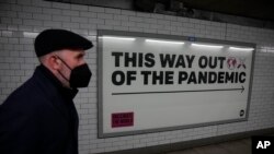 A man wearing a face mask to curb the spread of coronavirus walks past a health campaign poster from the One NGO, in an underpass leading to Westminster underground train station, in London, Thursday, Jan. 27, 2022. 