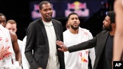 Injured Brooklyn Nets guard Kyrie Irving, right, puts his hand on fellow injured player Kevin Durant who smiles as he stands to greet teammates returning to the bench during a timeout in the second half of an NBA basketball game against the New York…